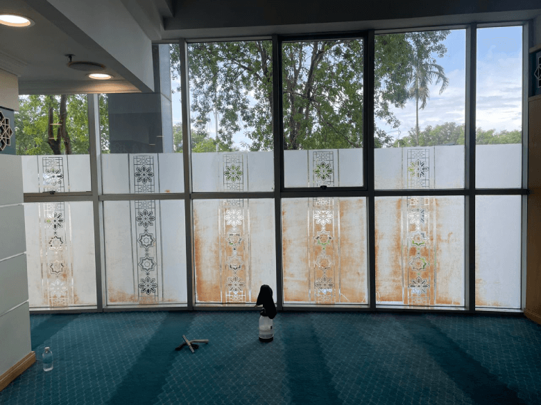 (FD) 252 - Frosted Window Film Kuala Lumpur Empty interior room with large frosted window panels; visible rust streaks on the glass and cleaning tools on a blue carpeted floor near a small air purifier/vent.