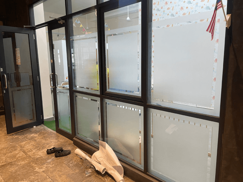 (FD) 254 - Frosted Window Film Kuala Lumpur Glass-walled office area with frosted windows, an open door, and shoes plus rolled paper on the floor in a tiled lobby area
