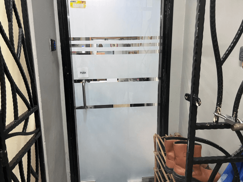 Glass door with frosted horizontal stripes and a push bar;'PUSH' on the left, boots on a rack to the right.
