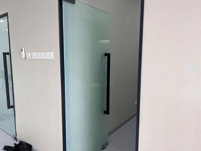 Frosted glass door with a black vertical handle in a modern office hallway.